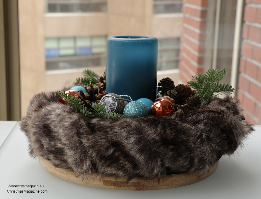 blue candle in fur wreath decorated with baubles, pine cones, and tree sprig